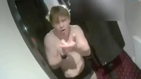 A screen shot of a young man wearing a pair of black underpants miming shooting a gun. 