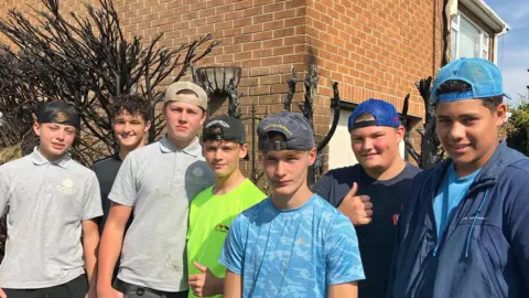 A group of boys stood in a line outside a house they saved from a fire