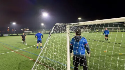 A footballer prepares to take a corner kick while defenders and the goalkeeper wait