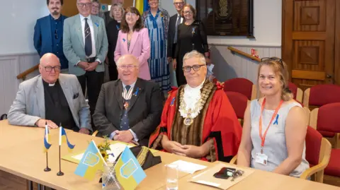 Robert Peel Four people sitting at a table in formal dress with small Ukrainian flags out with a small group behind them, all posing for the camera