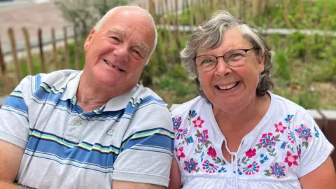 Steve Jones/BBC Married couple Graham and Julie Fidler. Mr Fidler has shaved grey hair, while Mrs Fidler has short grey hair. They are both smiling in the photo.