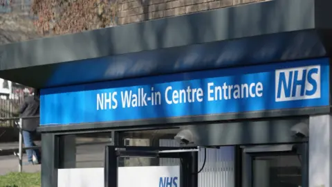 Sign of saying "NHS Walk-in centre entrance" in white on blue, with the NHS logo next to it 