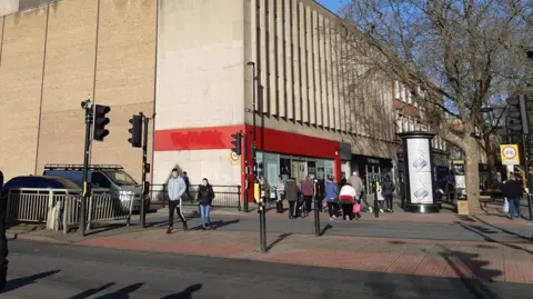 Local Democracy Reporting Service A large light beige bricked building on a high street in Peterborough. The front of the shop is outlined in red plastic with windows that have been covered up. 
