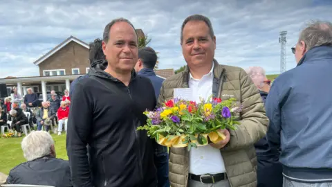 The brothers holding a floral wreath at the Slave Workers Memorial Ceremony