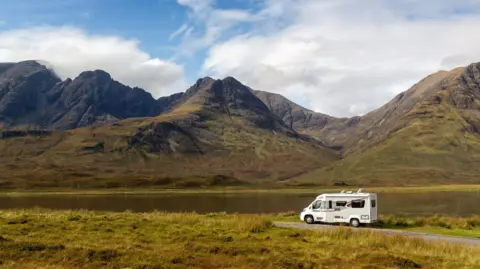 Getty Images A white campervan parked at the end of a gravel track by a loch and mountains on Skye. It is a fine, sunny day.