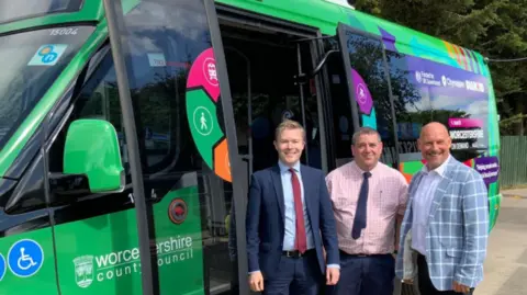 Worcestershire County Council Three men standing in front of a green minibus. They are wearing ties and jackets.