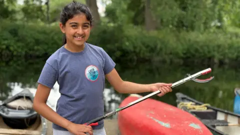 A 10-year-old girl in a purple t-shirt poses with her litter grabber.