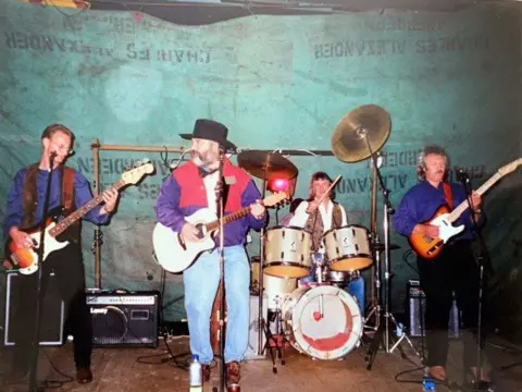 A band plays on board Hebridean Isles. A man in a cowboy hat plays guitar beside two other guitarists and a drummer.