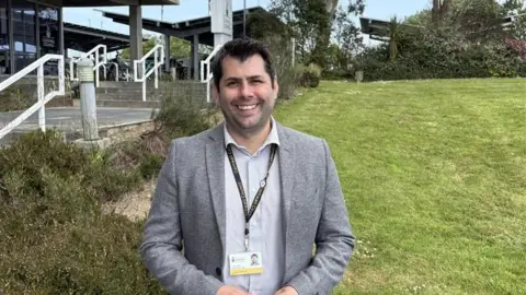 Leigh Frost weaning a suit jacket and shirt smiling in front of the Cornwall Council building