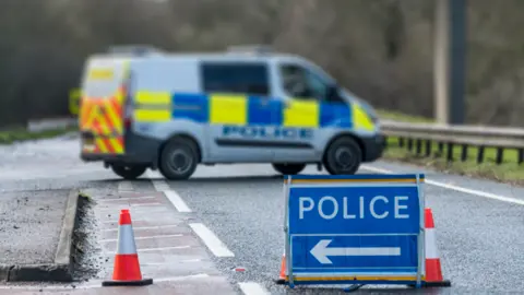 A police van and a cordon on a wet country road 