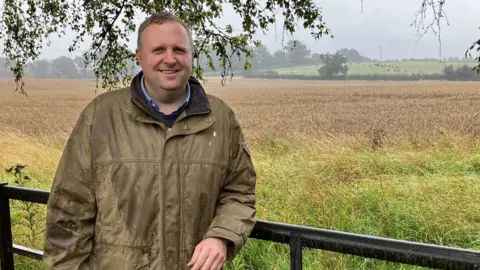 BBC Tom Collins standing in front of a field