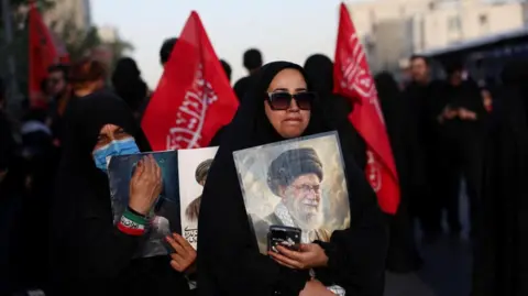 Reuters woman holds photo of Khamenei with red flags in the background