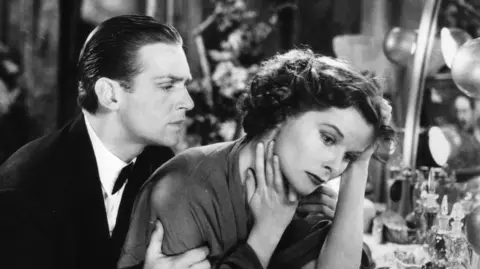 Getty Images Fairbanks Jr stood close to Katharine Hepburn on the set of Morning Glory in a black and white image.