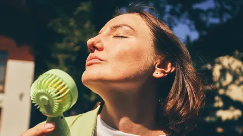 A woman cooling herself with a handheld fan.