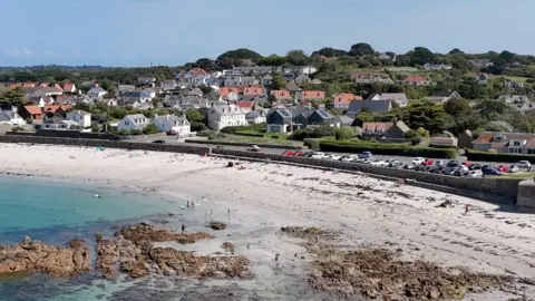 A drone view of Cobo bay showing the beach, roads housing and some of the designated parking. 