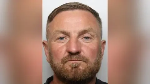 South Yorkshire Police A mugshot of Dylan White who has light brown hair, a beard and blue eyes. He appears slightly tanned and has wrinkles around his eyes.