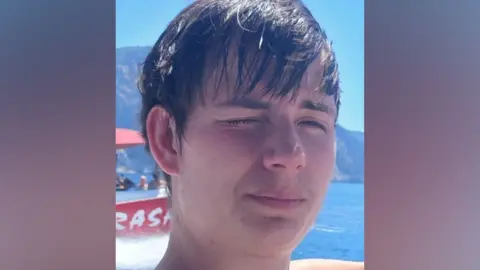 Family photo A man with dark wet hair squinting into the sun with water behind him