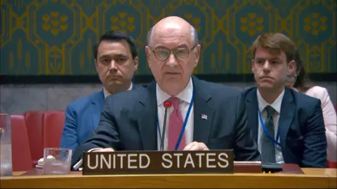 Man in a suit at a desk with 'United States' written below. 