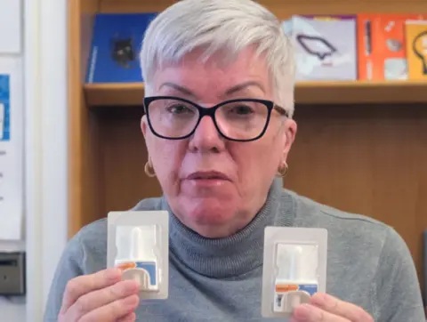 Dumfries and Galloway Health and Social Care Partnership Woman with glasses and grey hair holding two naloxone kits which are used to reverse the effects of opioid overdose. 