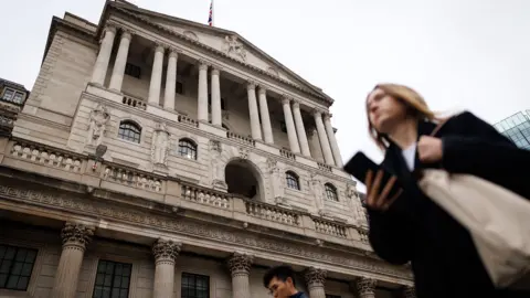 EPA The Bank of England is pictured against a grey sky with people walking in front holding their phones, in Bank, London in December.