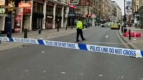 BBC Police tape across a road in west London, with a police officer walking in the background