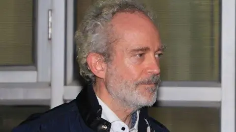 A photograph of Christian Michel, seen in white shirt and black jacket