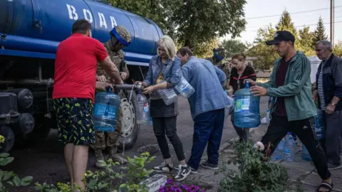 Persone riempiono bottiglie d'acqua fuori da una scuola utilizzata come rifugio antiaereo nella città di Sudza, controllata dall'Ucraina, il 18 agosto 2024.