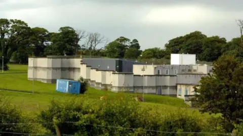 PA Media Landscape shot of Kerelaw residential school in Stevenston, North Ayrshire. The school is grey and white with a flat roof and is pictured behind a wire fence and hedge row, with a line of trees in the background.