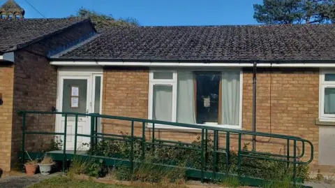 A house with a ramp to the front door. Two pieces of paper are taped onto the door.