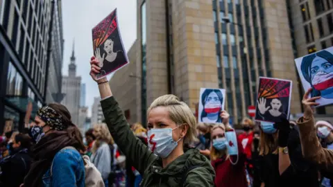 Omar Marques via Getty A woman wears a protective face mask and holds a banner as she participates in a National strike for the seventh day of protests against the Constitutional Court ruling