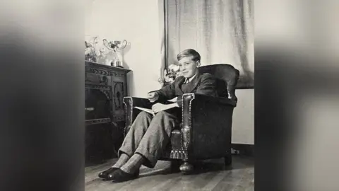 May Family Michael May as a young boy sitting in an armchair next to a trophy