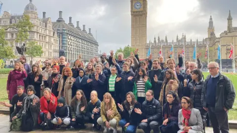 BBC Image showing attendees holding up their hands with the names of dead children on them