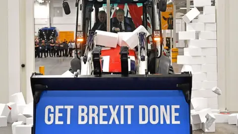 Getty Images Boris Johnson driving a JCB knocks down Brexit sign