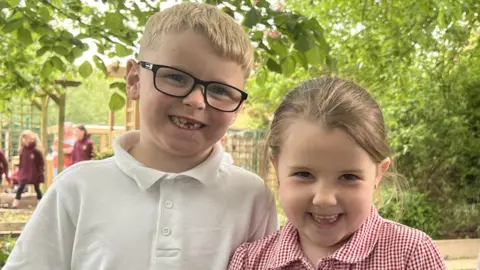 The children, a boy and two girls, are smiling at the camera. They were friends of Elias and enjoy coming to the garden in his memory. 