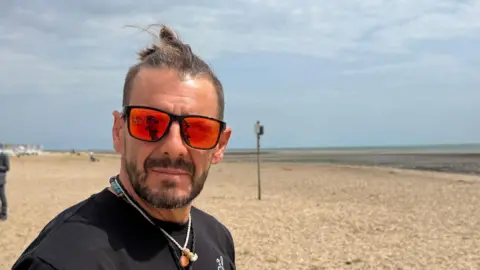 A man wearing sunglasses and a black shirt while standing on the beach.