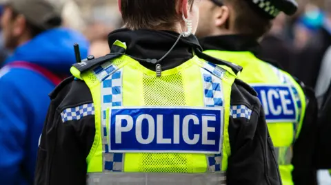 Police officers with their back to the camera wearing high visibility yellow vests