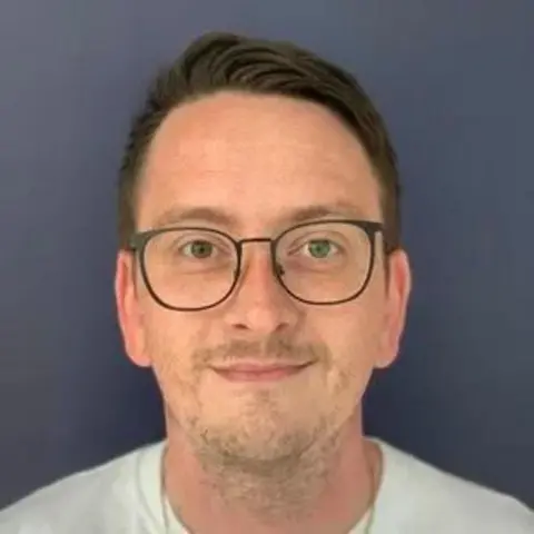 Liam Grimes Liam Grimes - a man in a white t-shirt and glasses