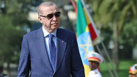 Turkey's President Recep Tayyip Erdogan in a dark blue suit and wearing sunglasses as he walks by a guard of honour in Ethiopia.
