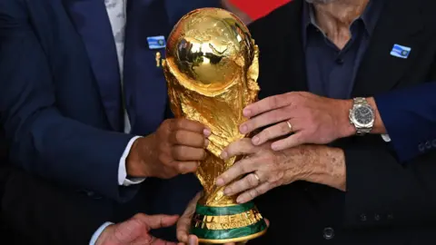 Four hands hold the gold World Cup trophy.