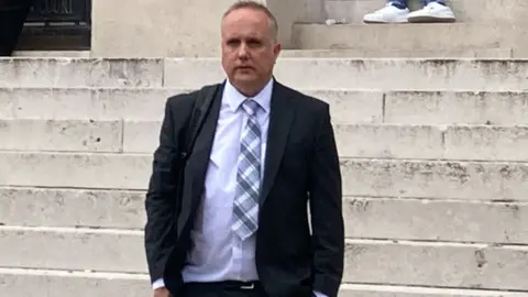 Dylan Dawes walking down the court steps. He's wearing. suit with a chequered tie.