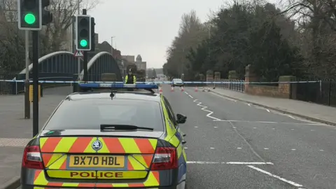 Leicester Media Online Police car by tape cordon which seals off a road going over an urban bridge