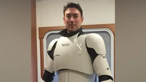 Sandeep Mohan James Taylor dressed in a classic Stormtrooper suit with a helmet under his arm.