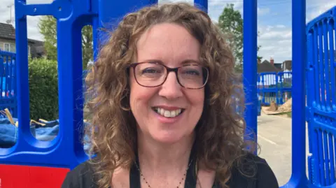 Louise Lee smiling at the camera has brown framed glasses and curly brown hair.