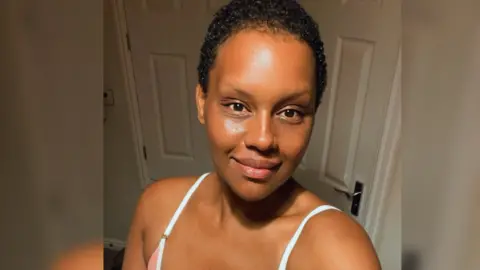 Rhakima Khan Rhakima , a black woman with short hair smiling at the camera