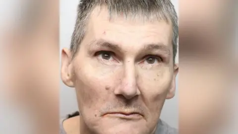 A police custody shot of Scott Thomson, who has short cropped grey hair and brown eyes.