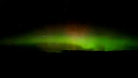 Tammy Hine The Northern Lights in the sky showing a green and red glow on a dark landscape. 