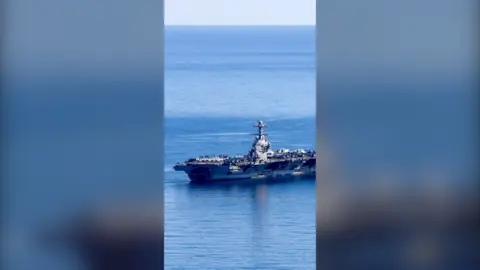 A large grey warship on open water with many military aircraft on board.