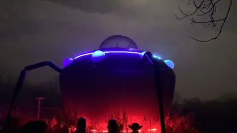 UFO-style accommodation pod lit up at night with red and purple lights shining out