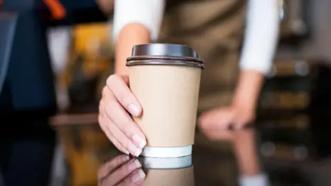 Getty Images Woman's hand holding a brown paper cup with black lid