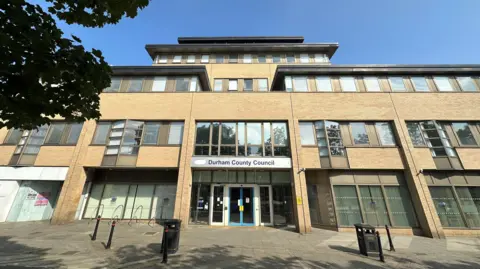 Exterior of Crook Civic Centre, the top floor of which is home to the coroner's service. It is a large building with yellow bricks and large windows, and a pagoda style roof.